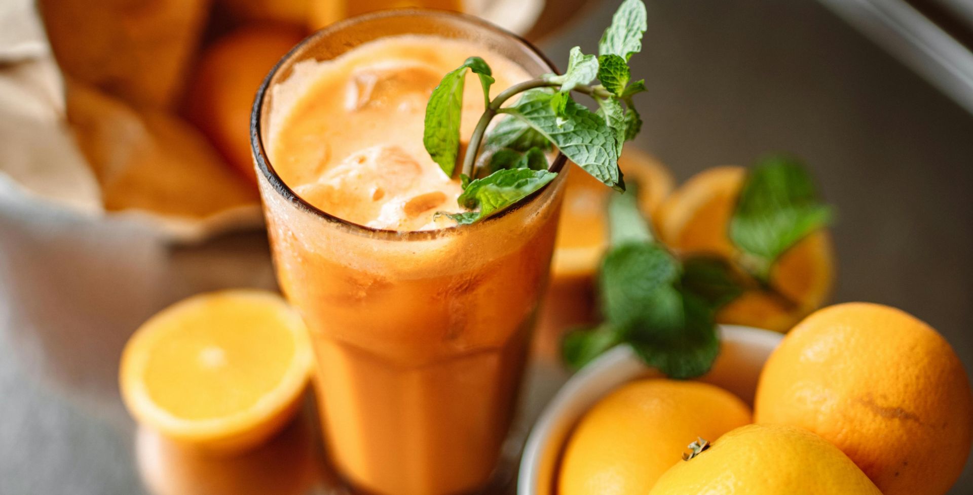 Orange juice garnished with mint surrounded by fresh oranges, perfect for a healthy refreshment.