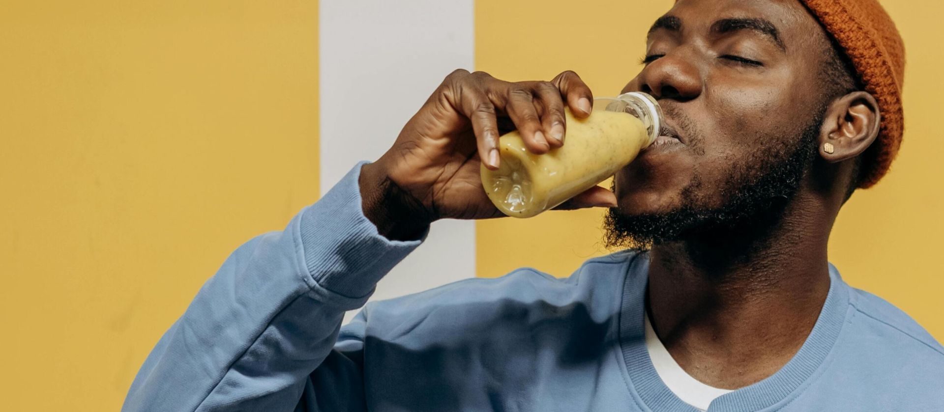 Casual man in blue sweatshirt drinking healthy juice with a cheerful expression.