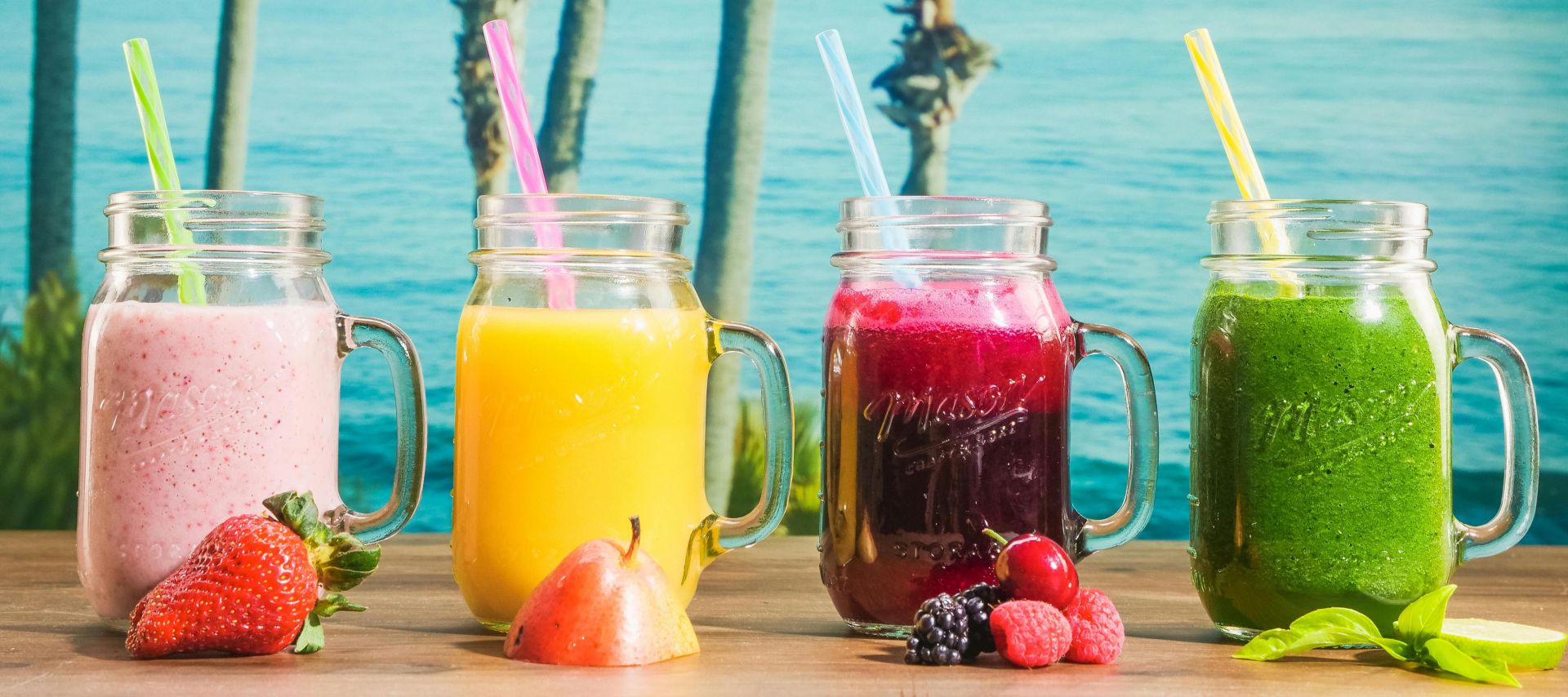 Vibrant smoothies in mason jars with a tropical ocean backdrop, perfect for refreshment.
